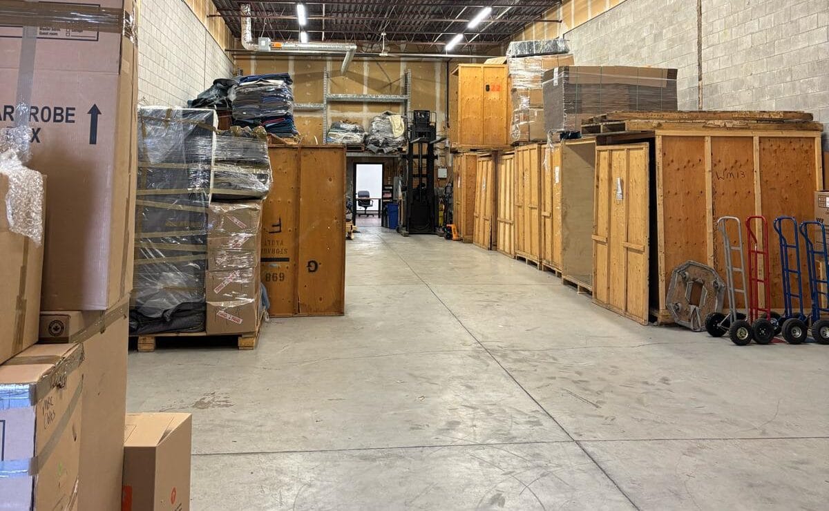 Warehouse aisle with tall wooden crates and stacked pallets on both sides, several hand trucks lined up to the right.
